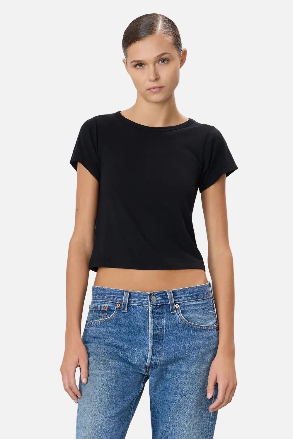 Person wearing a black crop top and blue jeans on a light gray background